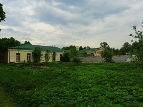 желтые одноэтажные домики с зеленой крышей на территории цветущего яблоневого сада с теплицами и ульями