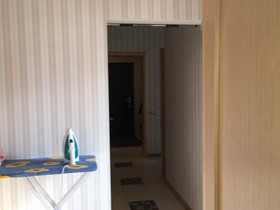 узкий коридор с турником между стен, квадратной бежевой плиткой на полу из открытой двери светлой комнаты с утюгом на синей гладильной доске у стены с полосатыми обоями