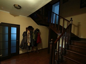 настенная и напольная вешалки с одеждой под лестницей в прихожей семейного дома в глухом лесу
