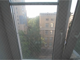 соседние дома сквозь прозрачную гардину на окне спальной комнаты простой сталинки 90-ых