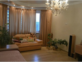 мягкий бежевый диван с подушками у большого окна с бежевыми шторами с современной квартире