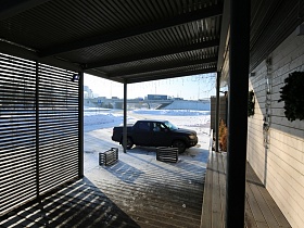 машина на снегу у открытой террасы с жалюзи под навесом светлого ресторана на берегу озера