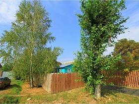 старая голубая дача СССР у поля за высоким деревянным штакетником в окружении высоких зеленых деревьев