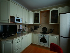 белая кухня и белый холодильник в светлой комнате большой трехкомнатной квартиры после перезда в многоэтажном доме