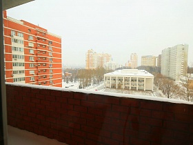 открытый кирпичный балкон под снежной шапкой через окно современной квартиры в переезде ( въезде) молодоженов в жилом доме
