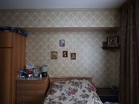 шкаф для одежды, комод и кровать под цветным покрывалом в коричневых цветах в спальной комнате с иконами на стене и в красном углу семейной классической сталинской трехкомнатной квартиры