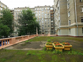 цветочные клумбы на площадке за светлым бетонным резным забором перед сталинским зданием с полисадником и пандусом