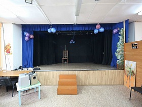 приставные ступени на театральную сцену с синим и черным занавесом, украшенной яркими воздушными шарами в сельском клубе