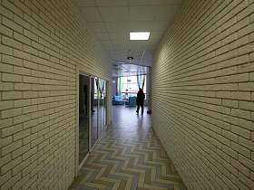 бежевые кирпичные стены длинного коридора и белый потолок на входе в просторный Лофт Бар в спальном районе