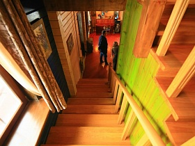 деревянная лестница с перилами между большой гостиной с камином посередине и комнатами в мансарде современного загородного дома