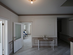 небольшой столик на белых фигурных ножках у открытой двери на кухню из просторного вестибюля в светлых тонах