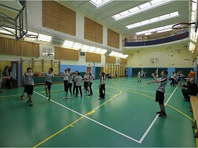 ученики школы на занятиях по баскетболу в современном спортивном зале с деревянными щитами на высоких стенах