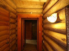 бра на бревенчатой стене небольшой комнаты с массивной деревянной луткой на дверях