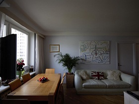 белые пушистые подушечки на белом мягком диване у стены с большой картиной,стулья со спинками вокруг деревянного стола у окна светлой гостиной стильной современной трехкомнатной квартиры