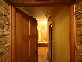 стены выложенные диким камнем у открытой коричневой деревянной двери из просторной зонированной кухни стильной современной квартиры