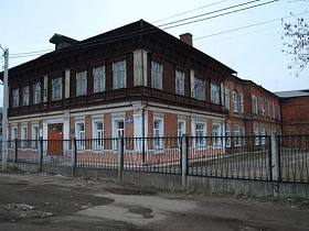 двухэтажное кирпичное двухцветное здание старинной школы за металлическим забором