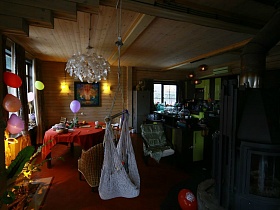белый гамак и разноцветные шары на дверном проеме столовой с бра и картиной на стене, круглым столом с красной скатертью в гостиной современного загородного дома