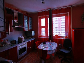 вишневая кухня с овальным обеденным овальным столом у окна обычной трешки стандартной высотки
