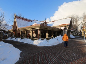 ресторан в купеческом стиле из бревен с треуголными крышами, открытой террасой под навесом на огромной площади, выложенной плиткой в зимнее время