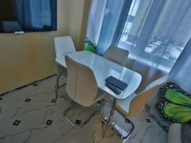 лаковый столик с дизайнерскими металлическими стульями у окна просторной кухни в молодежной евро квартире Новостроя