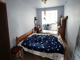 мягкий пуфик, деревянная кровать, покрытая синим покрывалом с белыми звездочками и зеркало над гриммерным столиков в спальне простой разрисованной семейной квартиры