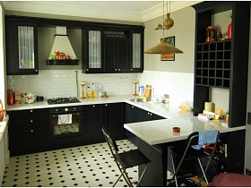черный барный столик и черного цвета кухня с белой рабочей поверхностью на полу с бело-черной плиткой в отдельной зоне стильной однокомнатной квартиры жилого дома