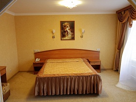красивое покрывало на большой кровати гармонирует с цветом стен и штор на окне номера гостиницы
