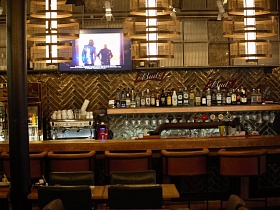 витрина с многочисленными бутылками сверху деревянной полки и фужерами на держателях снизу за барной стойкой стильного крафтового ресторана
