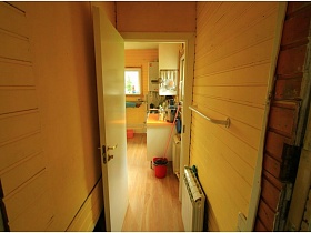 открытая дверь в кухню со светлой мебелью и колонкой у окна стильной дачи