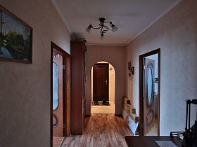 обувь на коврике у входной двери в прихожей через арочный дверной проем длинного коридора с картиной на стене и книжным шкафом яркой трехкомнатной квартиры