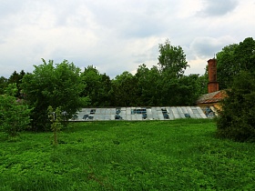стеклянная крыша просторной теплицы с разбитыми стеклами на территории цветущего яблоневого сада с ульями