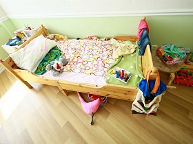 вещи и сумка на спинке детской неприбранной кровати, разнообразные игры и игрушки на стуле и на полу детской комнаты современной женской квартиры в жилом доме