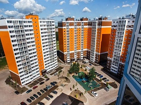 красивые ярко оранжевые и белые цвета стен многоэтажных домов новостройки с детской площадкой, размеченными газонами вдоль домов, парковочными местами на придомовой территории