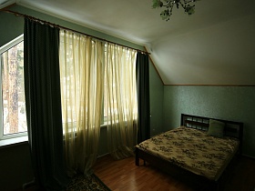 большая деревянная кровать в спальне с зелеными стенами, зелеными шторами и зеленым ковром съемного двухэтажного дома в соснах