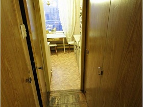 табурет и обычный обеденный прямоугольный стол у окна с белыми шторами кухни из открытой двери узкой прихожей квартиры панельного дома  СССР 80-89 гг стиля