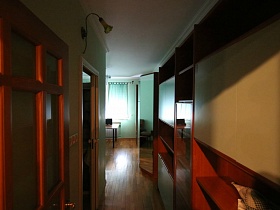 коричневый шкаф с бежевыми дверцами, открытыми полками в длинном коридоре с бра над открытой дверью в ванную комнату