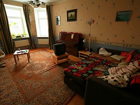 детский деревянный столик, телевизор на деревянной тумбочке, коричневое пианино, разложенный диван с подушками в гостиной с бежево-серыми обоями современной семейной квартиры