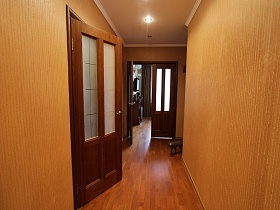 коричневые межкомнатныне двери со стеклянными вставками в узком коридоре со светло-коричневыми обоями на стенах трехкомнатной квартиры государственного служащего