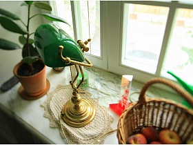 плетенная корзина с яблоками, настольная лампа и комнатный цветок на широком подоконнике окна однокомнатной квартире жилого дома