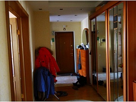 большой шкаф купе с зеркальными дверцами и одежда в углу коридора трехкомнатной квартиры