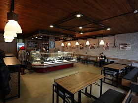  стеклянная витрина с готовой кулинарной продукцией в центре просторного стильного уличного кафе с большими окнами, с деревянными столами, креслами и скамейками по периметру