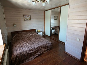 трехдверный шкаф-купе с белыми дверцами и зеркалом посередине, белая прикроватная тумбочка в светлой спальне просторного деревянного дома