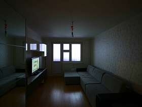 гостиная после ремонта с обычной лампочкой на белом потолке и светлыми обоями на стенах, мебелью и мягким диваном в большой трехкомнатной квартире после переезда