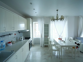 белая мебельная стенка, белый холодильник у балконной двери, белые стулья вокруг обеденного стола в зоне кухни стильной квартиры блогера на 7 этаже жилого дома