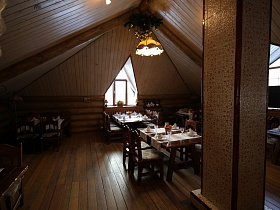  стулья со спинкой у сервированных столов из натурального дерева на деревянном полу уютной комнаты на мансарде под треугольной крышей ресторана в купеческом стиле
