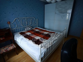 белый шкаф для одежды и белая кровать с фигурной металлической спинкой в голубой спальне актерской трехкомнатной квартиры