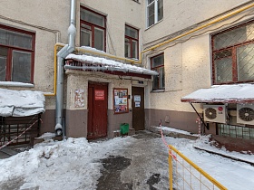 расчищенная дорожка от снега к деревянной двери подъезда в углу сталинского дома с кремовыми стенами и деревянными окрашенными рамами на окнах