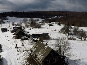 вид сверху на деревянные дома заброшенной деревне в зимнее время в окружении леса