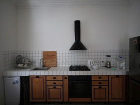 коричневая деревянная кухня с белой плиткой на рабочей поверхности и на столешнице в зонированной комнате современной скандинавской квартиры