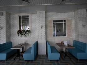 уютные индивидуальные зоны отдыха с голубыми диванчиками вокруг прямоуголных столиков у белой кирпичной стены с окнами в Лофт Баре